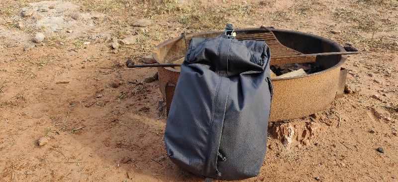 Dark gray Millican backpack proppoed up against a fire pit