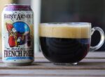 Saint Arnold French Press beer can on table next to clear glass coffee mug full of dark beer