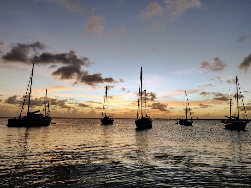 Ocean sunset with 6 moored sailboats bobbing on the water