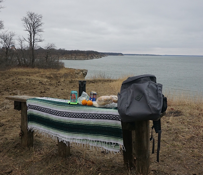 picnic spread next to backpack on wooden bench