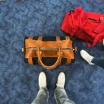 Black duffel bag with light brown leather trim on MIA airport carpet