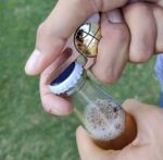 metal divot tool being used to open a glass Corona beer bottle