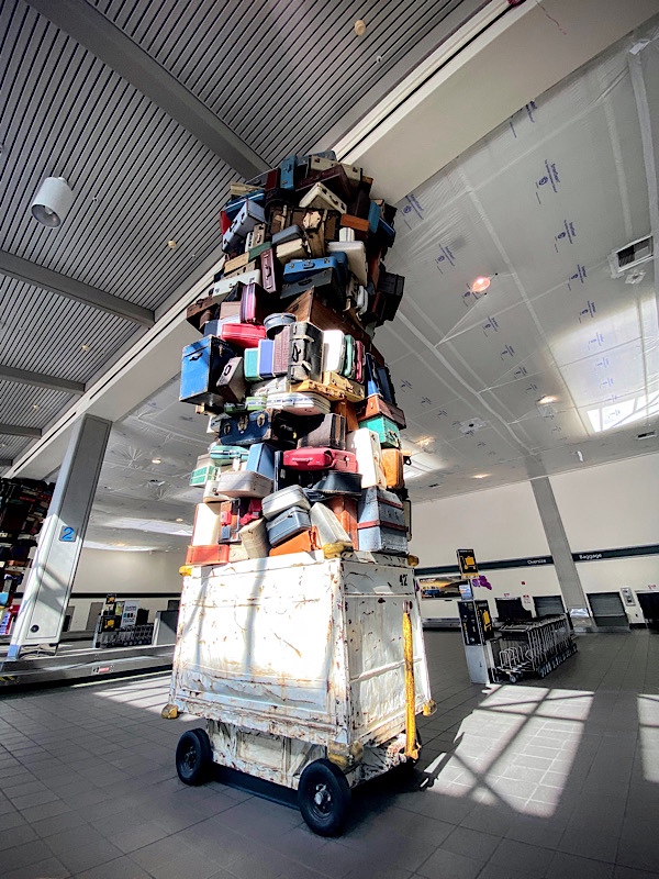 art sculpture at SMF airport baggage claim with hundreds of suitcases piled on top of a white baggage cart