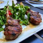 two grilled lamb lollipops over a bed of arugula
