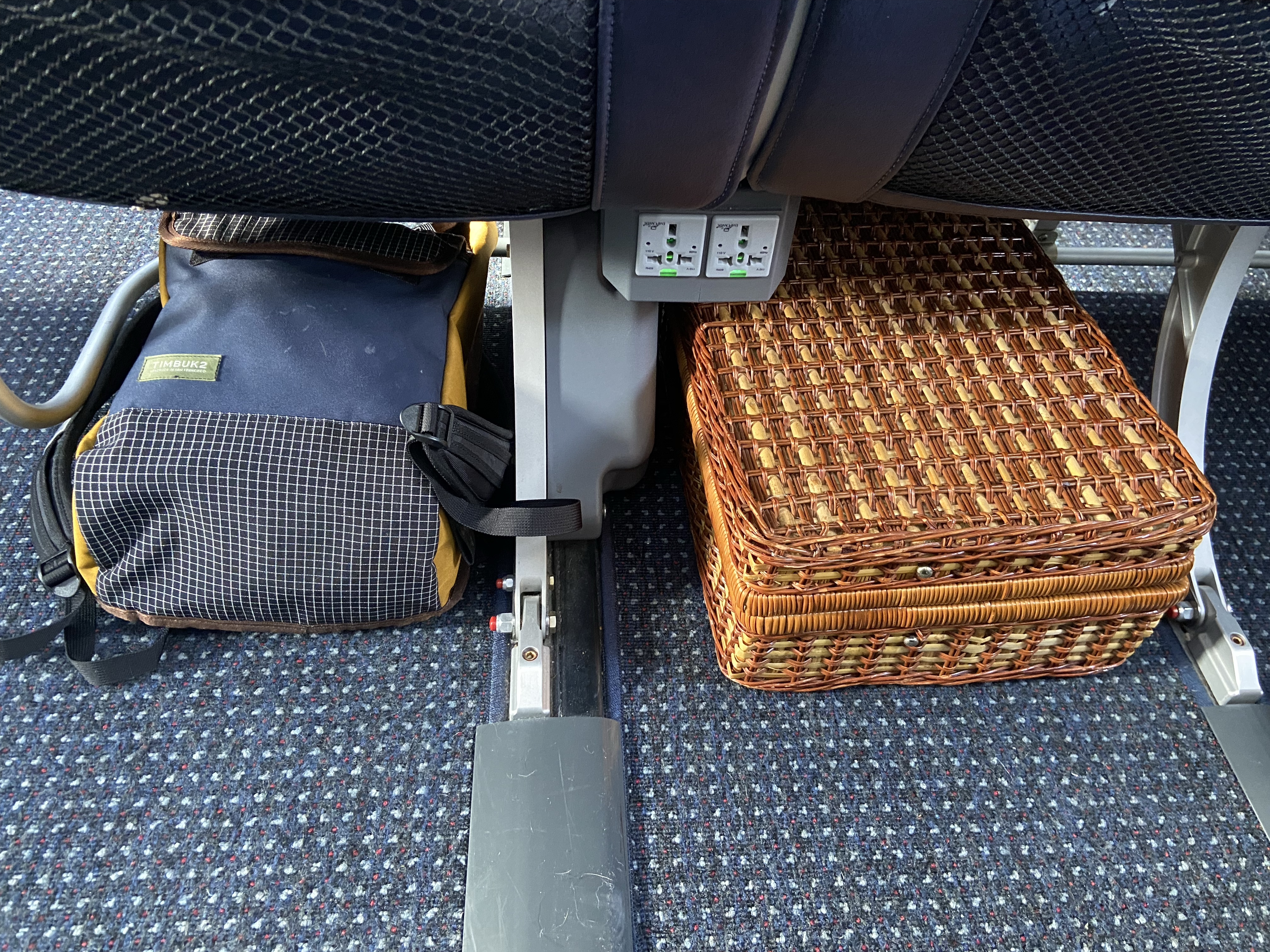 Timbuk2 Mini Prospect backpack & a wicker suitcase stowed under an airplane seat